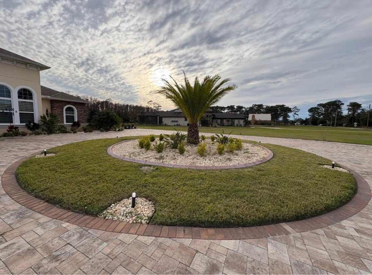 Circular landscape island with palm tree and white decorative stones in a paver driveway